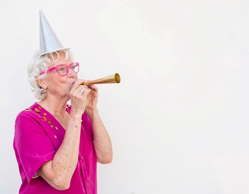Senior Woman in Party Hat Blowing Gold Horn