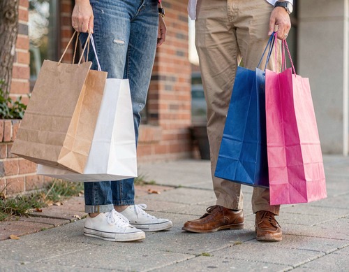 Two Shoppers with Paper Bags Outside Brick Building