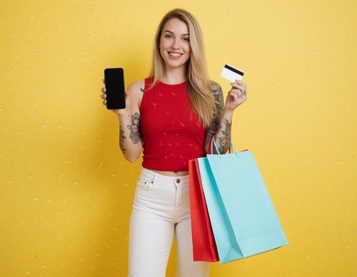 Woman Holding Credit Card, Smartphone and Shopping Bags Against Yellow Background