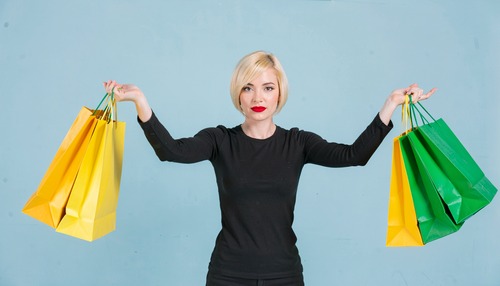 Smiling Woman Holding Yellow and Green Shopping Bags Against Blue Background