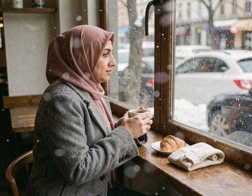 Woman in Hijab Sipping Coffee by Snowy Cafe Window