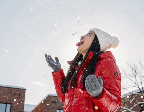 Young Asian Woman Catching Snowflakes in Red Puffer